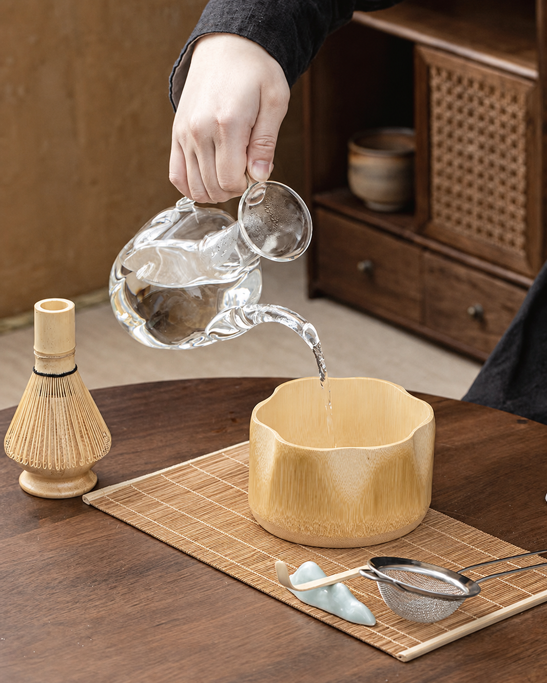 Pouring water into a bamboo matcha bowl on a bamboo placemat